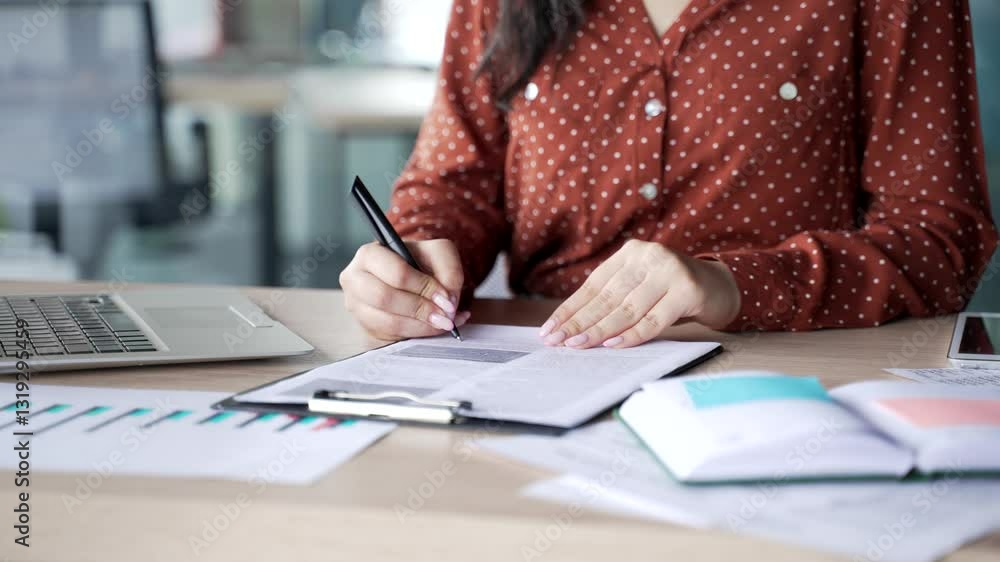 Close up of a female hand signing documents at a desk at a workplace in a modern business office. Young businesswoman boss looks through the folder with documentation and signs the contract with a pen Close up of a female hand signing documents at a desk at a workplace in a modern business office. Young businesswoman boss looks through the folder with documentation and signs the contract with a pen
