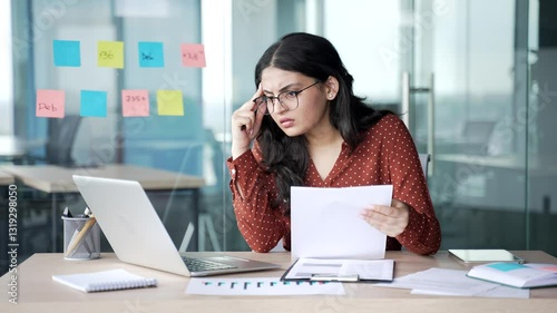 Confused young businesswoman having difficulty with paper work checking documents on laptop computer sitting at workplace in business office. Frustrated female financier unhappy with financial results