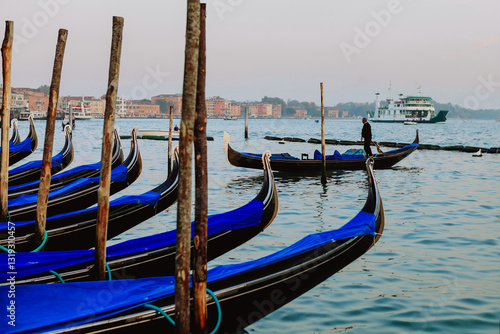 Street photos of Venice, Italy. Blue coloured Gondola boats lined up as they are berthed alongside wooden poles