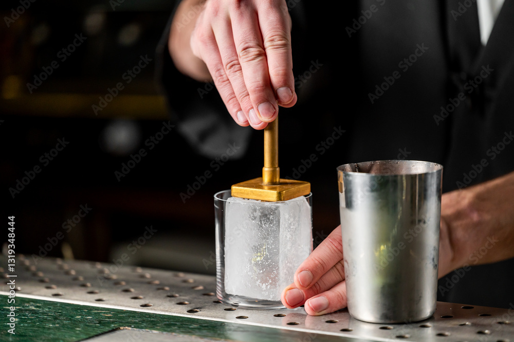 Obraz premium A bartender using an ice press on a large ice block to create a perfectly shaped ice for cocktails at a bar.