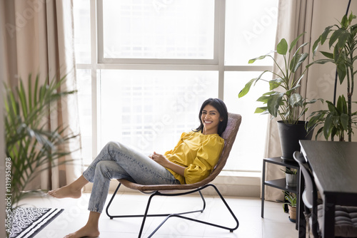 Canvas Print Relaxed Indian woman sit comfortable on cozy armchair looking at camera with joy