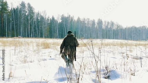 A lone hunter with a gun is walking through a winter forest.  Tracks down wild forest animals and hunts them. Hunting animals is a way of human life.