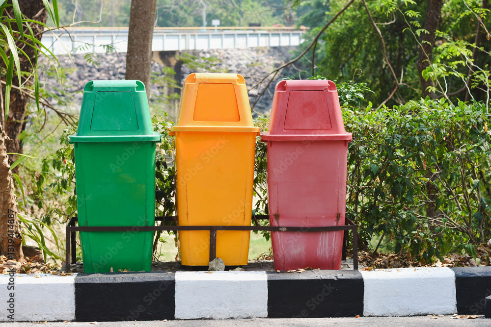 The bins are colored green, yellow, and red, and are placed on a black-and-white striped curb. They are secured in a metal frame. The bins are colored green, yellow, and red, and are placed on a black-and-white striped curb. They are secured in a metal frame.