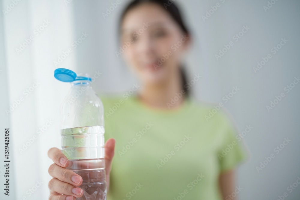 Woman holding a water bottle indoors while smiling in natural light during daytime Woman holding a water bottle indoors while smiling in natural light during daytime