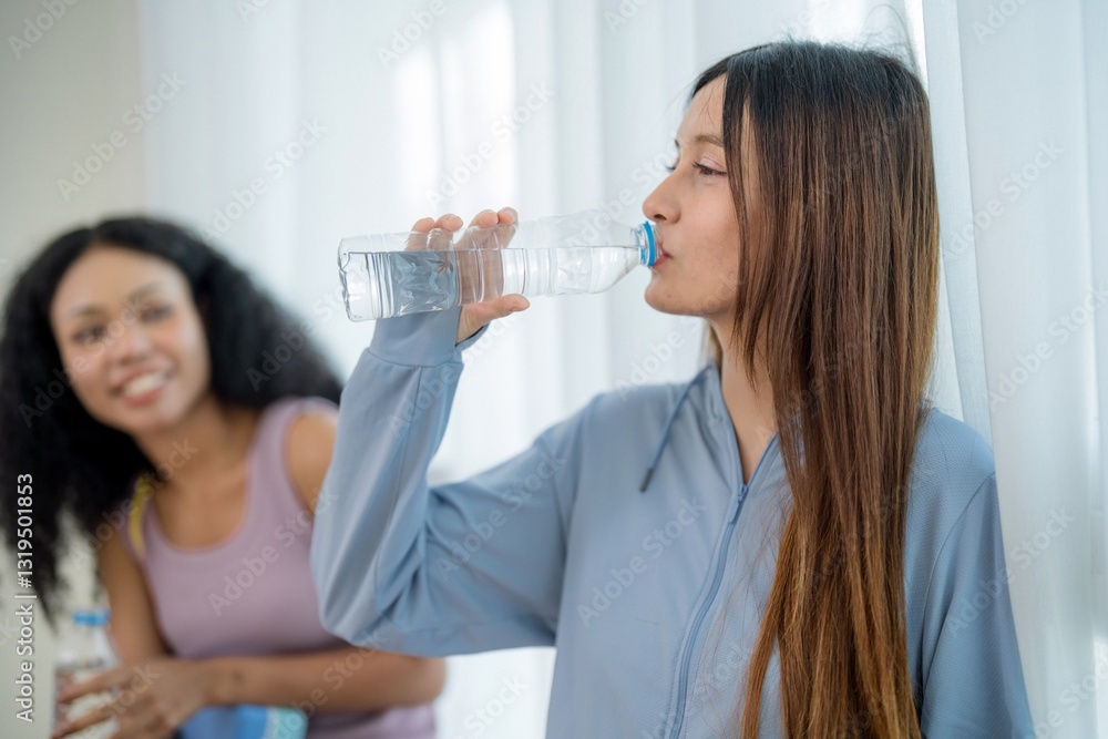 Young women enjoying a fitness break while hydrating in an indoor environment during a sunny afternoon Young women enjoying a fitness break while hydrating in an indoor environment during a sunny afternoon