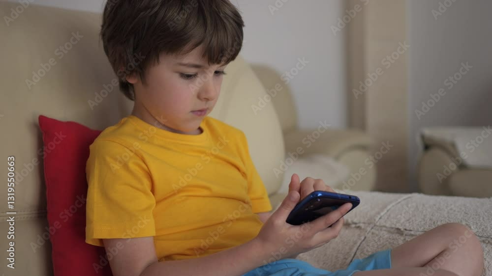 Child Browsing Social Media. Portrait of Cute Boy Playing Game on Smartphone Relaxing in Living Room. Child Using Mobile Phone, Sitting on Sofa at Home, Homeschooling, Distant Remote Education. Child Browsing Social Media. Portrait of Cute Boy Playing Game on Smartphone Relaxing in Living Room. Child Using Mobile Phone, Sitting on Sofa at Home, Homeschooling, Distant Remote Education.