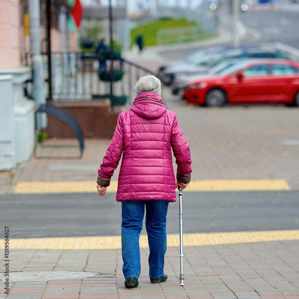 Elderly woman in pink jacket walking with cane on city sidewalk, mobility support and independence for senior citizens in an urban environment. Senior woman using cane for balance while walking street