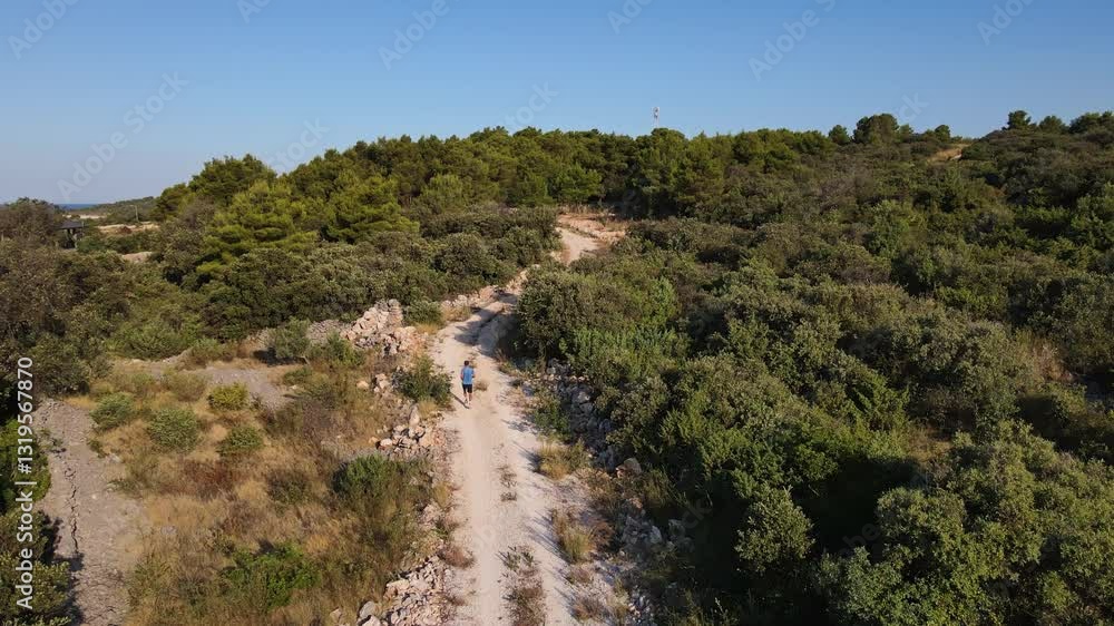 Man jogging on dirt trail in hot sunny day, surrounded by lush green nature, aerial view. Professional athlete training endurance outdoor. Trail running and fitness concept