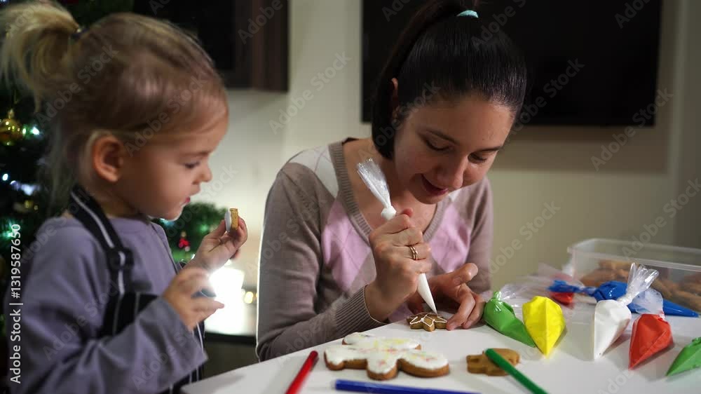 Little girl looks after her mother decorating a cookie with icing from a pastry bag