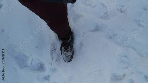 POV video of walking through fresh snow shows snow-covered winter boots and a serene snowy landscape. 4k video 39 seconds. Burgundy pants and soft blue light enhance the calm, wintry forest or park