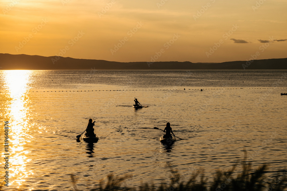 Fototapeta premium Magical sunset over Cres island, Croatia, with istrian peninsula visible across the sea while children enjoy riding their sup boards
