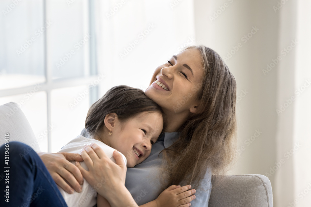 Warm embrace of mommy. Tender excited young mum nanny older sister relax on sofa at home hug beloved little daughter girl hold child in caring arms as kid snuggling up to her with smile. Copy space Warm embrace of mommy. Tender excited young mum nanny older sister relax on sofa at home hug beloved little daughter girl hold child in caring arms as kid snuggling up to her with smile. Copy space