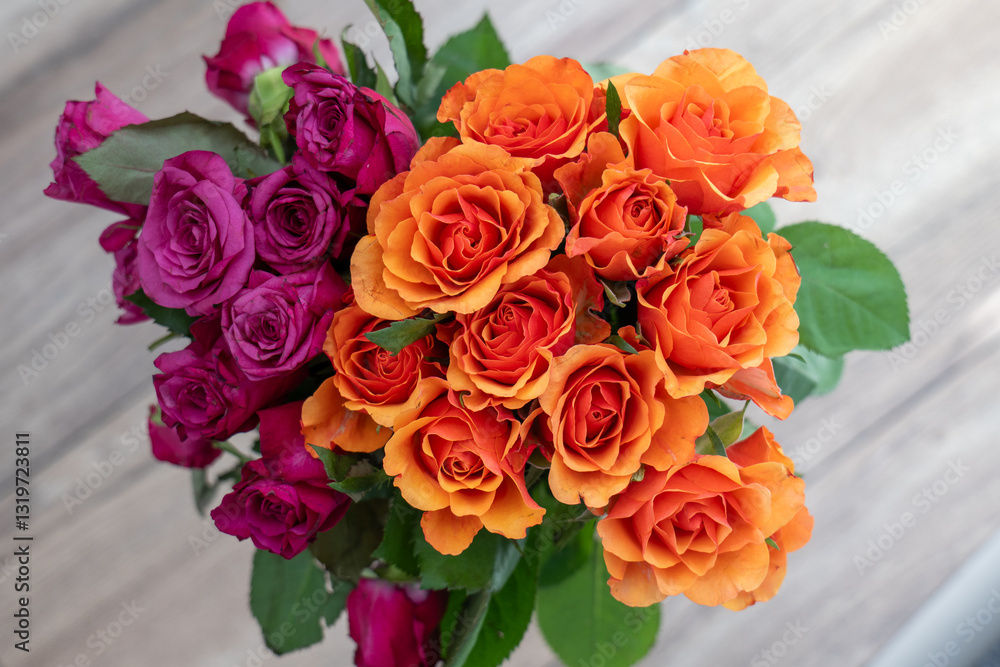 Obraz premium A bouquet of vibrant roses, one in deep purple and the other in bright orange. The roses are fresh and beautifully arranged on a neutral wooden background.