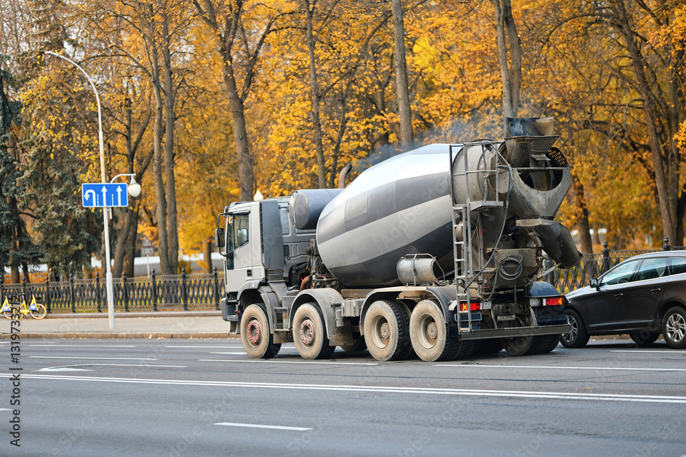 Cement mixer truck driving on an urban road in autumn, industrial transportation and construction logistics in city environment. Heavy duty concrete mixing truck moving through city streets.