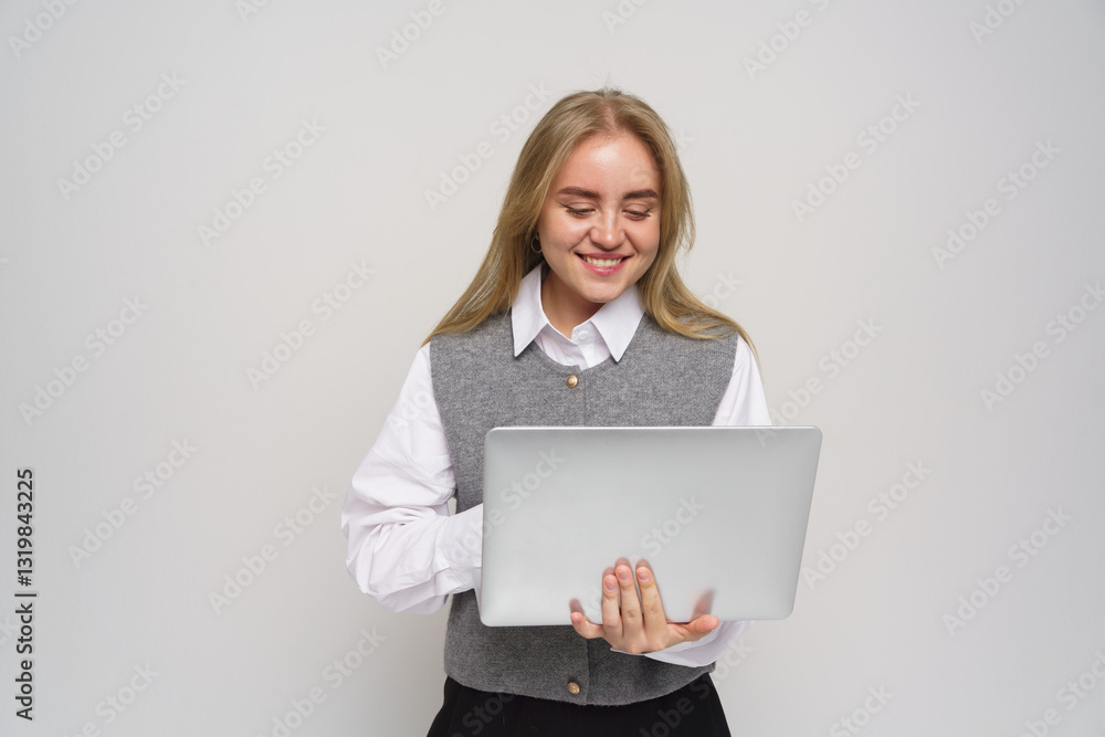 Young woman smiles while using a laptop in a simple, modern indoor setting Young woman smiles while using a laptop in a simple, modern indoor setting