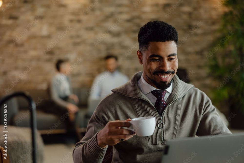 Smiling Professional Enjoying Coffee While Working on Laptop in Modern Office Smiling Professional Enjoying Coffee While Working on Laptop in Modern Office