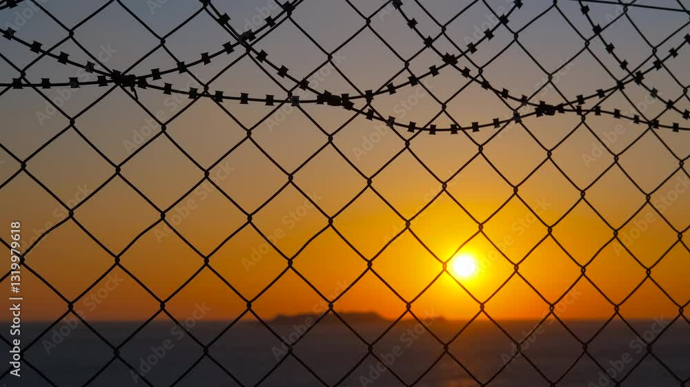 Setting sun through barbed wire fence. Golden sunset rays filtering through rusty barbed wire fence, soft clouds obscuring distant horizon, symbolizing confinement and fragile hope Setting sun through barbed wire fence. Golden sunset rays filtering through rusty barbed wire fence, soft clouds obscuring distant horizon, symbolizing confinement and fragile hope