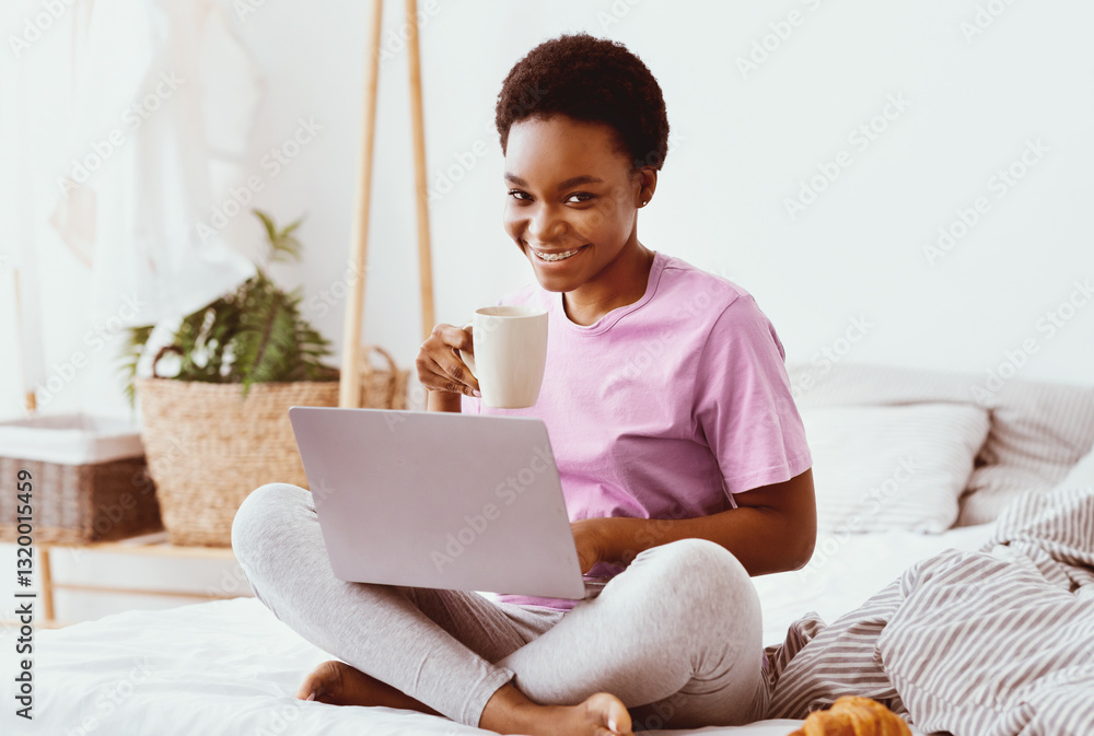 Remote work at home, blog, breakfast in bed with social media. Happy millennial african american female with cup of hot drink typing on laptop, with croissant in bedroom interior in morning free space Remote work at home, blog, breakfast in bed with social media. Happy millennial african american female with cup of hot drink typing on laptop, with croissant in bedroom interior in morning free space