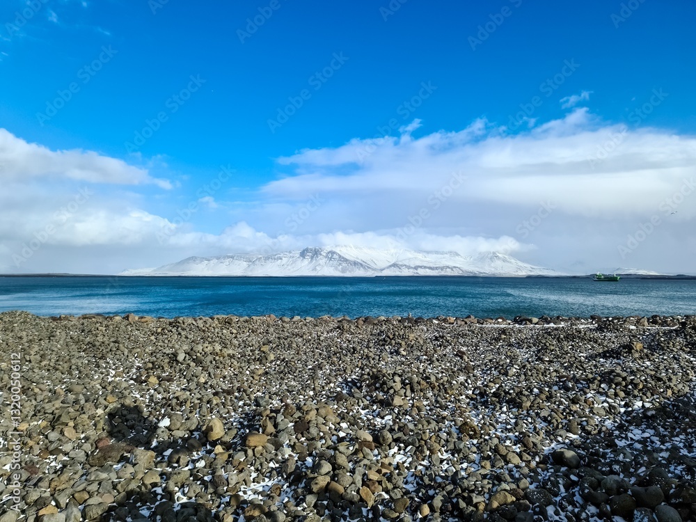 Rocky beach overlooking snowy mountains across blue sea in iceland Rocky beach overlooking snowy mountains across blue sea in iceland