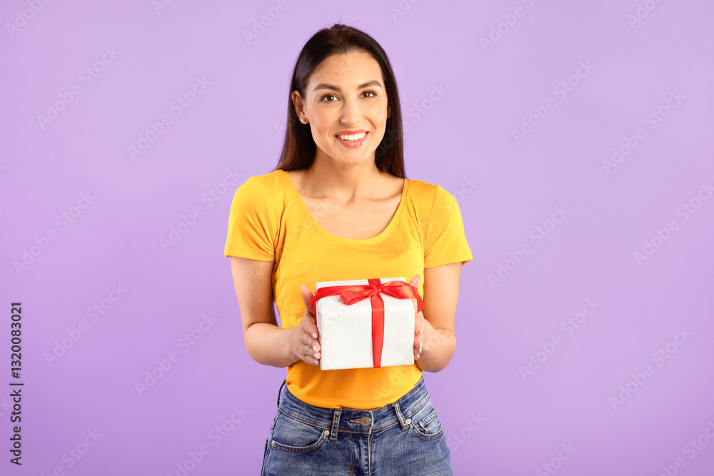 Holiday Concept. Portrait of smiling young woman holding wrapped gift box giving it to camera isolated over purple studio background. Happy lady greeting and celebrating special day Holiday Concept. Portrait of smiling young woman holding wrapped gift box giving it to camera isolated over purple studio background. Happy lady greeting and celebrating special day
