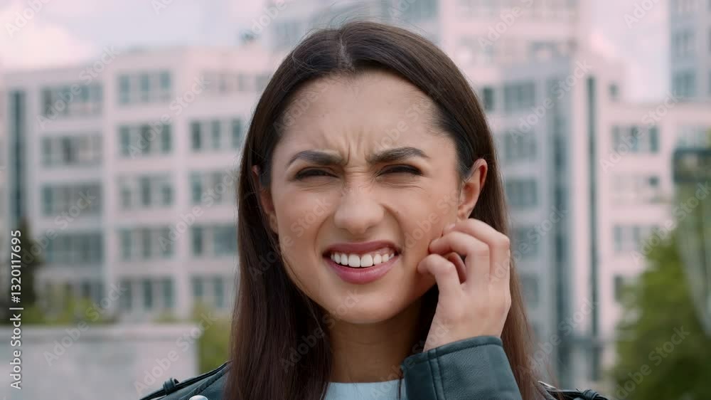 A young Arab woman is outside in a city setting, depicting casual street life. She has brunette hair and expresses curiosity, surrounded by modern buildings and green spaces.