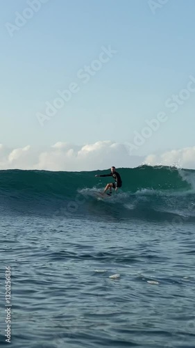 Vertical video of a young man surfing in the clear waters of the Indian Ocean on a sunny day.Bali island.Indonesia