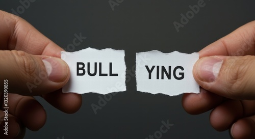 a person's hand tearing a paper with the words bullying written on it, a symbol of anti-bullying