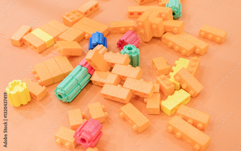 Obraz premium Colorful toy building blocks and balls scattered across a bright orange surface, creating a playful and abstract composition.