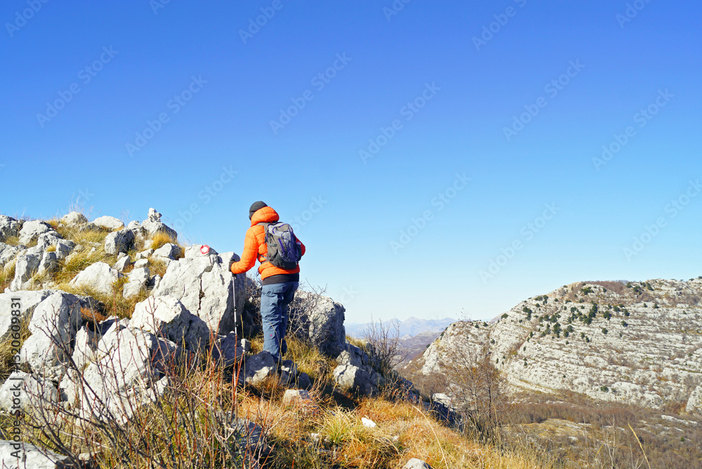 Achieving goals: a man photographed from behind with a backpack and hiking poles passes the final section on the way to the top. The traveler climbs the mountain along a marked path (Orjen, Montenegro Achieving goals: a man photographed from behind with a backpack and hiking poles passes the final section on the way to the top. The traveler climbs the mountain along a marked path (Orjen, Montenegro