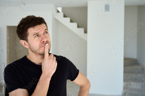 Thoughtful man in black t-shirt standing in new unfinished apartment, planning home renovation. Male home owner thinking about interior design after buying house