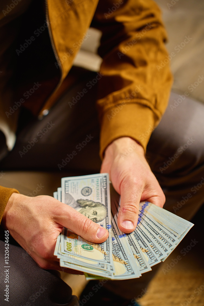 Close-up of man counting dollar banknotes at home. Person planning his personal finances, sitting on sofa with cash money. Concept of planning home budget, savings and personal finances