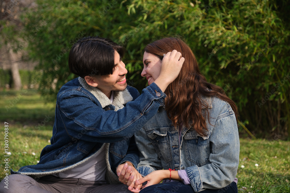 Fototapeta premium Romantic couple sitting on grass, holding hands and showing love and affection