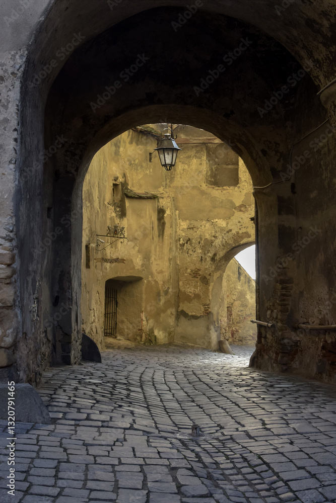 Obraz premium Arched passage with lantern over an old cobblestone street in ancient European city.