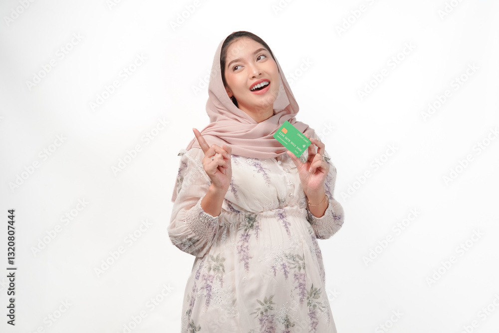 Attractive Asian Muslim pregnant woman holding card while pointing to the copy space behind.