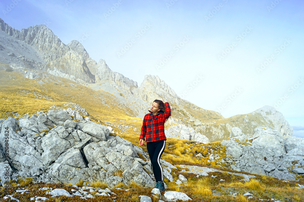 Naklejka premium Travel to the east of Montenegro: a full-length photograph of a female tourist under the peak of Kucki Kom during a hike in the Komovi Nature Park. Active recreation in autumn: a trip to the mountains