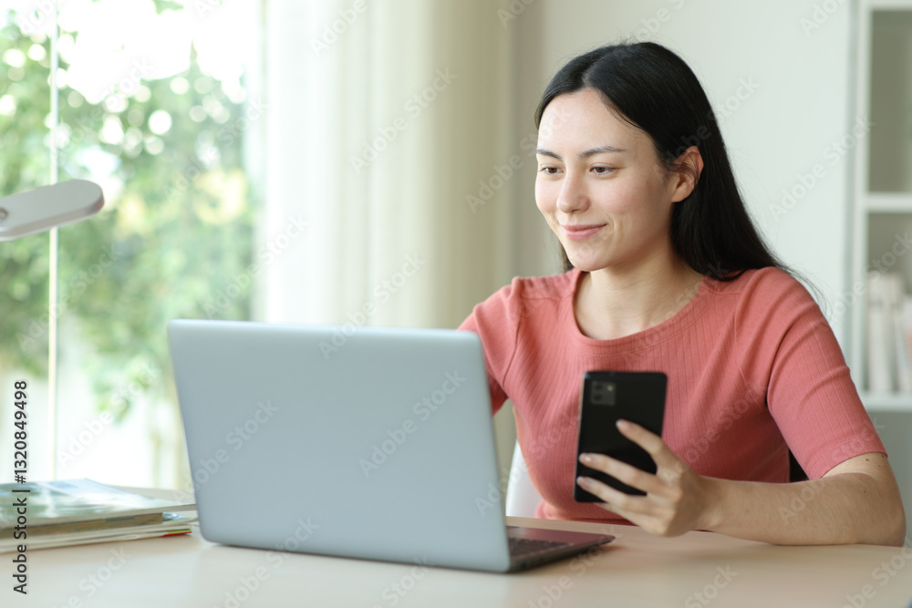 Satisfied asian woman using laptop and phone in a room Satisfied asian woman using laptop and phone in a room