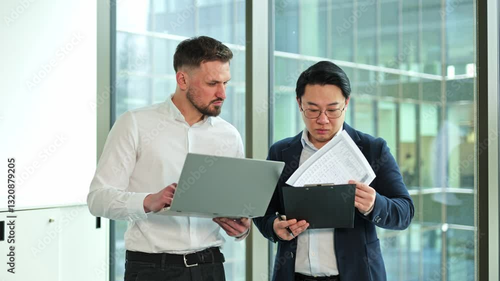 Two diverse businessmen collaborate on a project, reviewing documents and discussing strategies in a modern office with large windows. Two diverse businessmen collaborate on a project, reviewing documents and discussing strategies in a modern office with large windows.