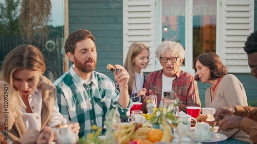 Camera view of family sitting at small table in garden. Talking with each other while enjoying delicious food. Friendly gathering. Visiting other family members in countryside. Warm evening.