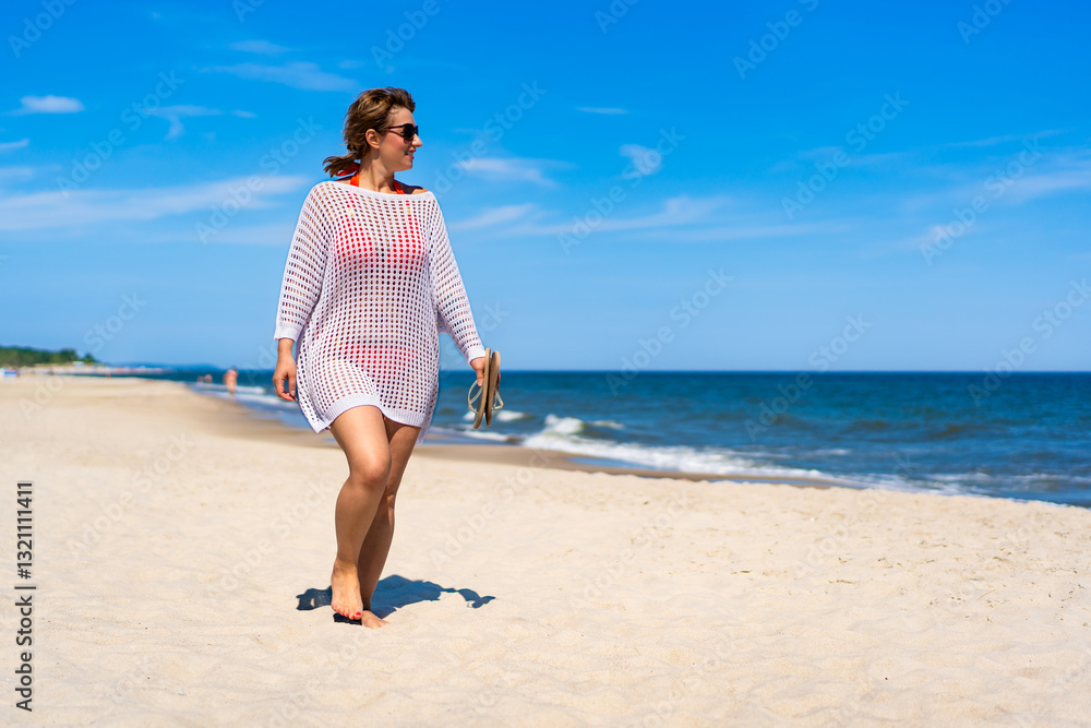 Summertime by sea. Beautiful middle aged woman sunbather walking on sandy beach on sunny summer day. Side view Summertime by sea. Beautiful middle aged woman sunbather walking on sandy beach on sunny summer day. Side view