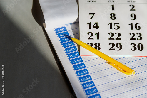 An organizer with an empty hourly schedule and a calendar next to a pen symbolizes planning for the future and self-discipline, control over time, and productive planning of tasks and meetings.