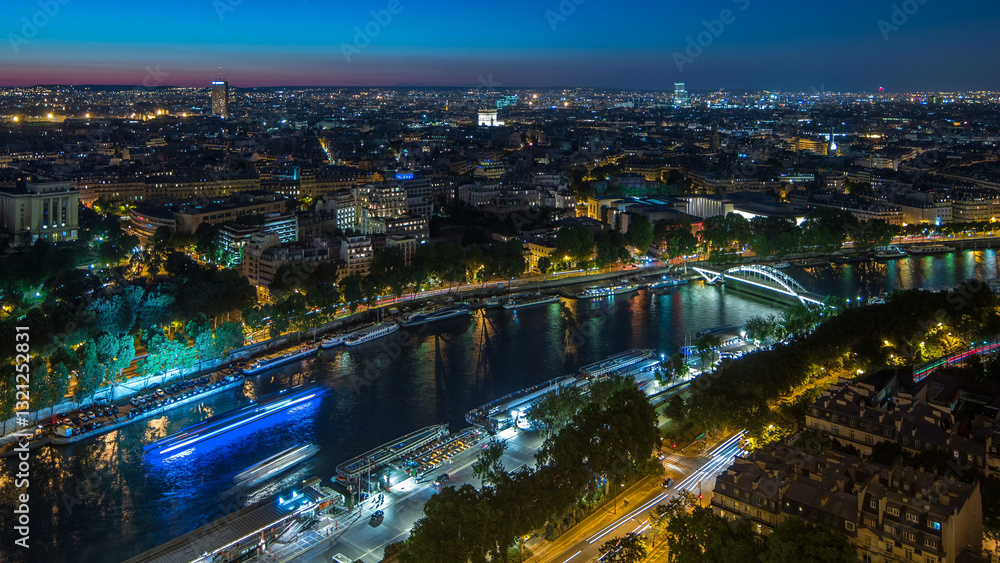 Fototapeta premium Aerial night timelapse view of Paris City and Seine river shot on the top of Eiffel Tower