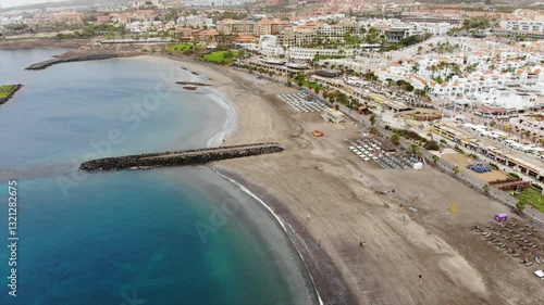 Aerial view of Costa Adeje city beach, Tenerife, Canary islands. Cinematic 4K video with sandy coast, clear turquoise waters of Atlantic ocean, villas, resorts, quay. Forward and side tracking shot