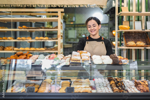 Billede på lærred Smiling baker arranging pastries in display case at bakery shop