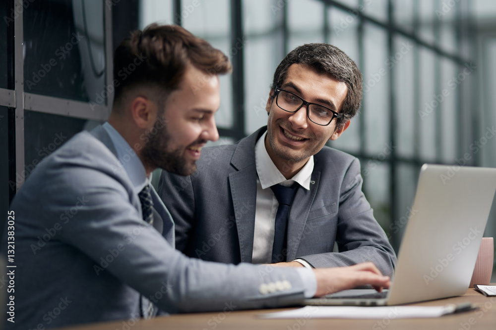 Fototapeta premium Two young businessmen sitting at workplace and working together in office