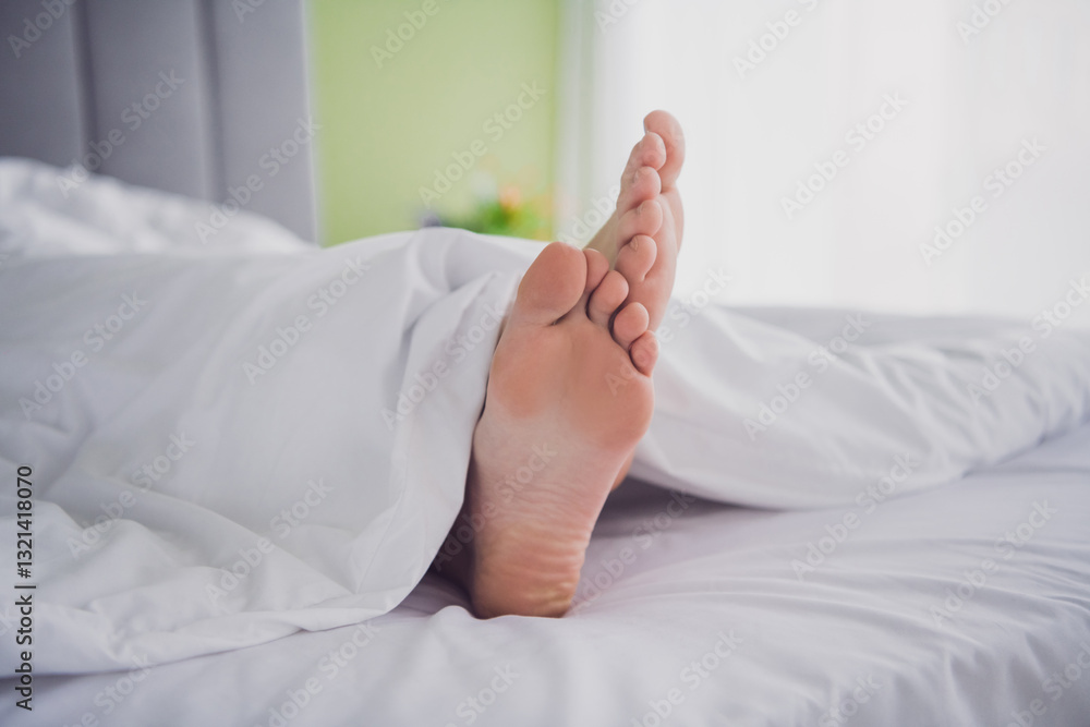 Close-up of bare feet sticking out from under the duvet in a cozy bedroom, symbolizing relaxation and comfort in a bright morning setting. Close-up of bare feet sticking out from under the duvet in a cozy bedroom, symbolizing relaxation and comfort in a bright morning setting.