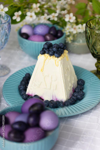Holiday laid table for Easter with Russian traditional dish called Easter made of cottage cheese, painted eggs in shades of lilac and purple with green blooming branch