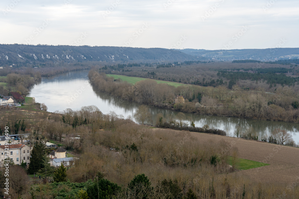 Obraz premium Beautiful view of the Seine River winding through La Roche-Guyon while trees stand bare in early spring under a cloudy sky