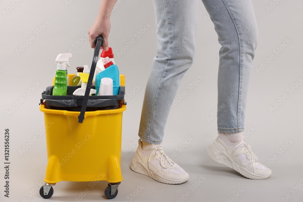 Woman with bucket of cleaning supplies on light background, closeup Woman with bucket of cleaning supplies on light background, closeup