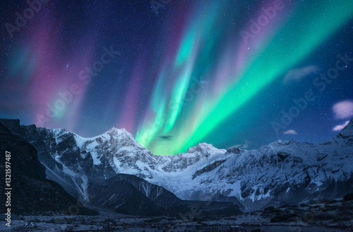 Fototapeta Naklejka Na Ścianę i Meble -  Northern lights over the snowy mountains at night in Lofoten, Norway. Aurora borealis above the snow covered rocks. Winter landscape with polar lights, mountain peak. Beautiful starry sky with aurora	