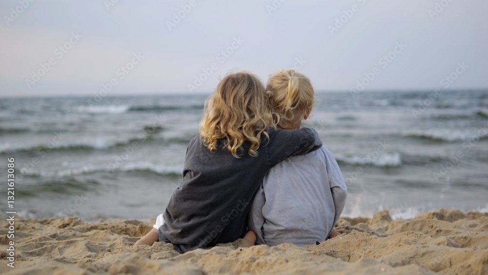 Fototapeta premium Young blonde siblings sharing tender moment on sandy beach, nestling close together while watching peaceful ocean waves during golden evening light. Concept Love between Sisters